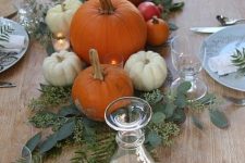 a Thanksgiving centerpiece of greenery, white and orange pumpkins and candles is a lovely idea for a rustic celebration
