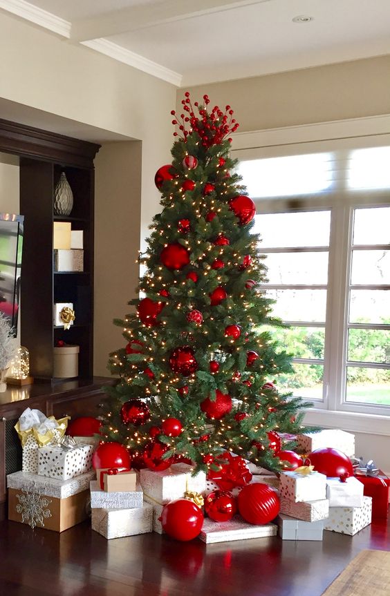 a bright Christmas tree with average scale and oversized red ornaments and lights plus berries on top is wow