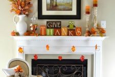 a bright Thanksgiving mantel with colorful leaves, colorful striped candles, bright cubes, dried leaf arrangements and blankets and pillows