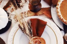 a bright boho Thanksgiving place setting with white plates, a rust-colored napkin with dried citrus slices and wheat