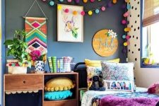 a bright kid’s room with a black wall, colorful pompom garlands, pillows, bedding and a rug is extra bold