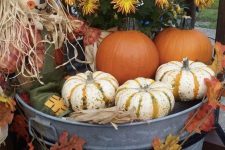 a bucket with bold blooms, leaves, pumpkins and a scarecrow is a pretty outdoor decoration for Thanksgiving