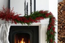 a chic Christmas fireplace with a mantel decorated with evergreens and red berries, with white stockings is a lovely idea