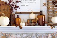 a chic and bold Thanksgiving mantel with white pumpkins, dark leaves, apothecary bottles, a quote and some wooden decor