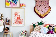 a colorful and fun boho-inspired kid’s room with colorful bedding and pillows, a colorful gallery wall with a hanging and some stools and rugs