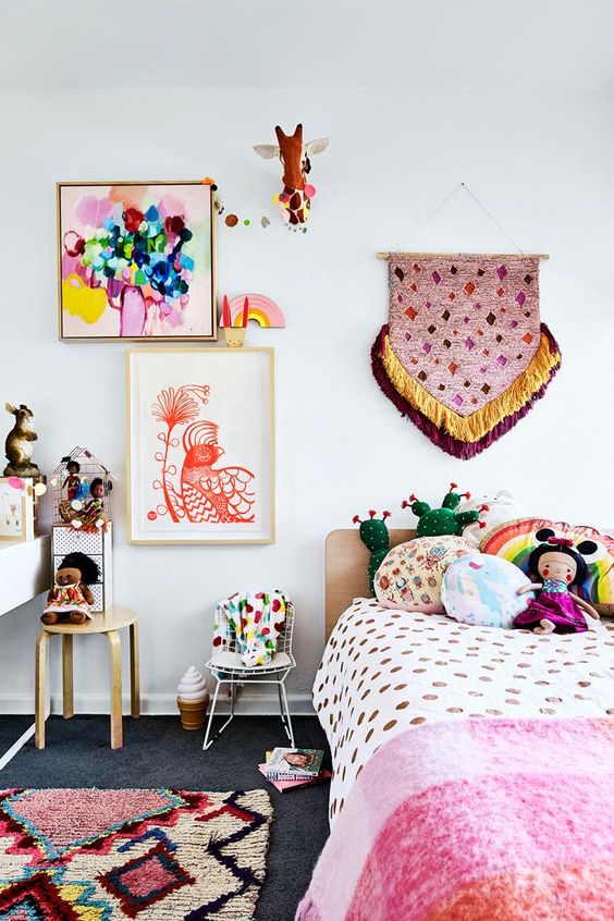 A colorful and fun boho inspired kid's room with colorful bedding and pillows, a colorful gallery wall with a hanging and some stools and rugs