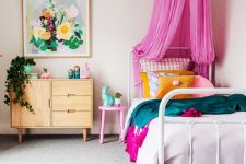 a colorful and welcoming kid’s room with a bed with colorful bedding and a hot pink canopy, a dresser, a pink stool and some floral artwork