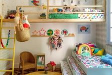 a colorful shared kids’ room with a raised bed and a bed at the window, some ladders, a wicker chair and colorful bedding and toys