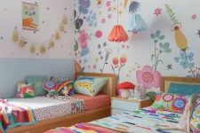 a colorful twin kid’s room with a floral statement wall, colorful bedding and pillows, pendant lamps and a tassel garland