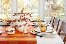 a cozy and simple Thanksgiving centerpiece of white pumpkins and bold berries accented with a bold matching table runner is a cool idea