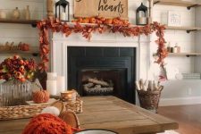 a cozy rustic Thanksgiving mantel with a bold leaf garland, orange pumpkins, a paper hanging and candle lanterns