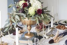 a dramatic Thanksgiving centerpiece of a gold bowl, white and purple blooms, greenery, blackberries and fruit