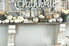 a faux Thanksgiving mantel with small neutral pumpkins, lots of window frames and a mirror plus a sign of metal