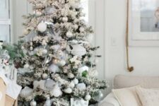 a flocked Christmas tree with white, silver and emerald ornaments, feathers, pinecones and grey ribbons is a lovely idea
