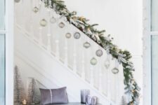 a flocked evergreen Christmas garland with lights and silver and light green ornaments to decorate the stairs