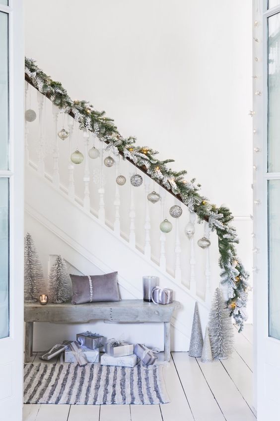 a flocked evergreen Christmas garland with lights and silver and light green ornaments to decorate the stairs