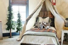 a gorgeous camp-themed kids’ room with canopy on branches, woven shades, faux trees and a faux fireplace