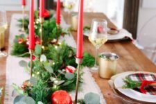 a lovely Christmas tablescape with an evergreen runner, silver, gold and red ornaments, red thin and tall candles and plaid plates