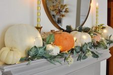 a lovely modern Thanksgiving mantel with greenery, white blooms and large natural pumpkins and candles