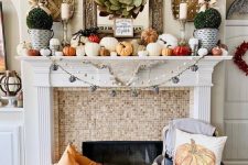 a lovely modern farmhouse Thanksgiving mantel with lots of pumpkins of various sizes, greenery topiaries, a leaf wreath and woden baskets