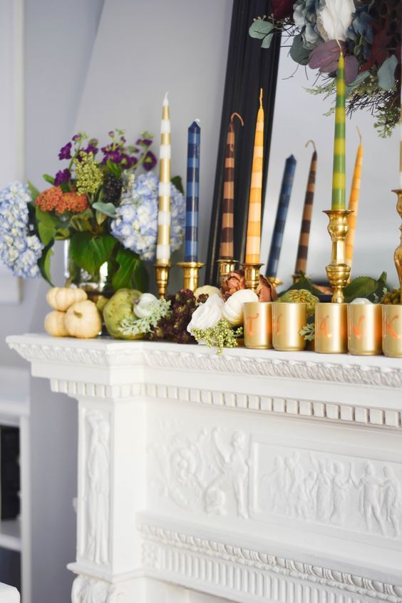 a modern and bright Thanksgiving mantel with real fresh veggies, greenery, bold blooms, bright striped candles and gold candleholders