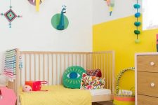 a modern colorful kid’s room with a color block yellow and white wall, bright bedding and a rug, cardboard taxidermy and accessories