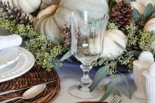 a neutral Thanksgiving centerpiece of greenery, candles, pinecones and neutral heirloom pumpkins is a chic idea