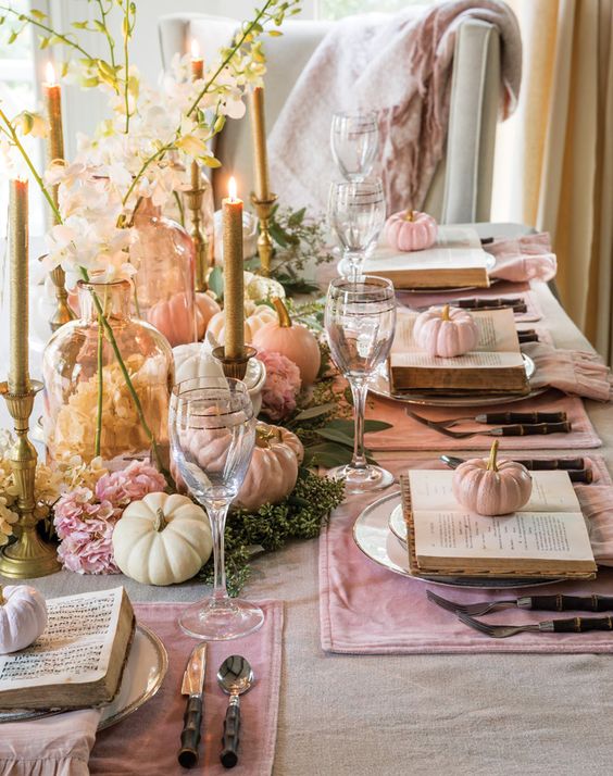 a pastel Thanksgiving centerpiece of pink blooms, greenery, pastel pumpkins and some amber vases and glitter candles is amazing