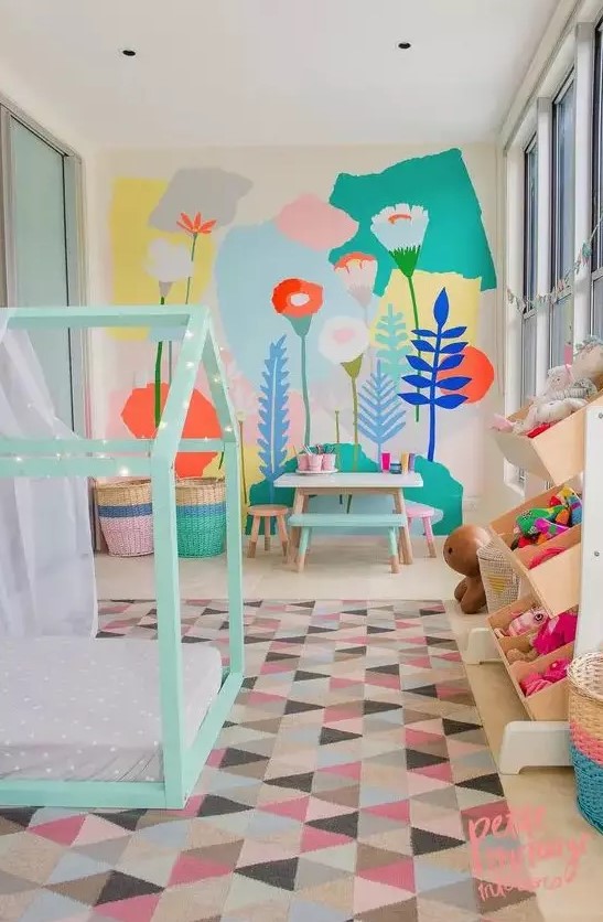 A pastel kid's room with a bright floral wall, a mint house shaped bed, colorful toys and a bold rug and baskets