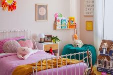 a pretty and bright kid’s room with scallop edge walls, a bed with bold pink bedding, a green pouf and lovely rugs, books and toys