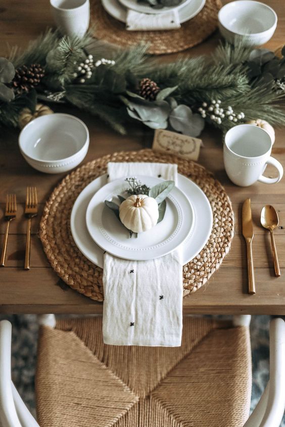 a pretty and chic Thanksgiving place setting with a woven placemat, white porcelain, a printed napkin, a pumpkin and some leaves is pure chic