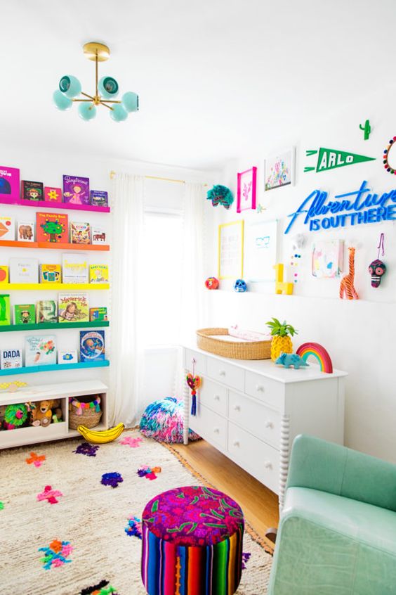 A rainbow inspired kid's room with colorful ledges and books, a bold gallery wall, a green leather rocker, a colorful pouf