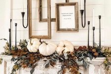 a refined vintage Thanksgiving mantel with lots of greenery and dried leaves, white pumpkins, white candles and empty frames for a farmhouse touch