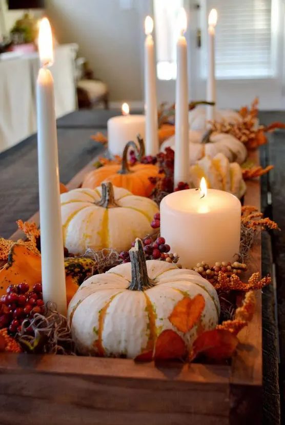 a rustic Thanksgiving centerpiece of a wooden box, berries, dried leaves, pillar and tall candles and some gourds is a cool idea