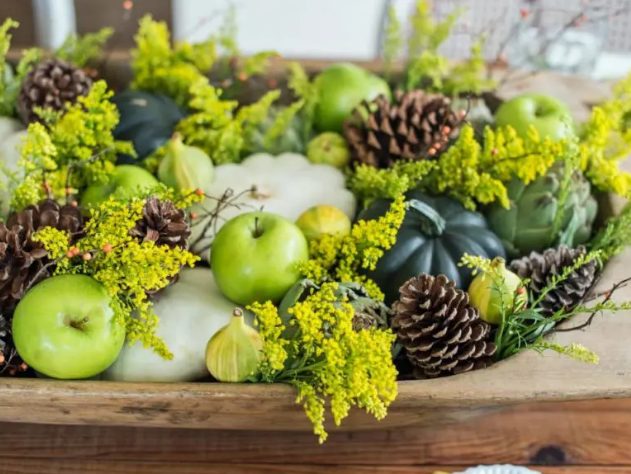 a rustic Thanksgiving centerpiece of a woodne box with blooming branches, green apples, pinecones and dried and fresh veggies