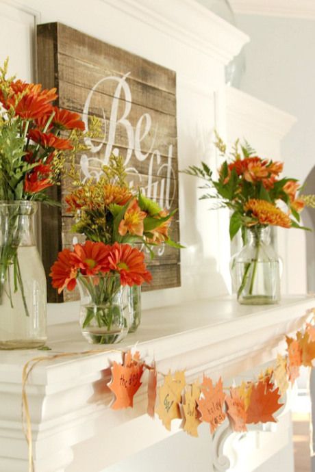 a rustic chic Thanksgiving mantel with bold blooms and greenery arrangements, a wooden sign and paper fall leaf garland