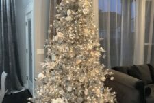 a silver Christmas tree with lights, white and silver ornaments, fabric blooms and silver gift boxes is a stylish and bold idea