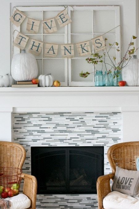 a simple Thanksgiving mantel with oversized white pumpkins, bright apples, branches with leaves and burlap banners