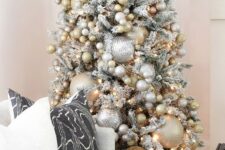 a snowy Christmas tree with oversized and smaller metallic Christmas ornaments plus lights