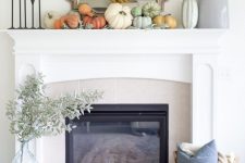 a stylish modern Thanksgiving mantel with a leaf wreath, neutral and pastel pumpkins and large vases