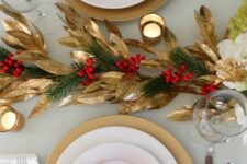 a stylish red and gold Christmas table with gold foliage, evergreens and berries, red blooms and candles