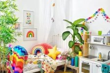 a super bold kid’s room with rainbow color garlands, matching bedding, blankets and pillows, a colorful rug and artworks