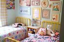 a super fun and bright shared kids’ room with light green walls, yellow beds with colorful bedding, a bright gallery wall and toys