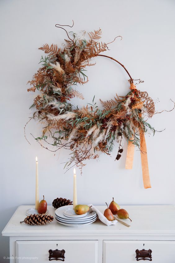 a unique and super textural Thanksgiving or fall wreath of pampas grass, greenery, dried leaves, pinecones and long ribbons is amazing