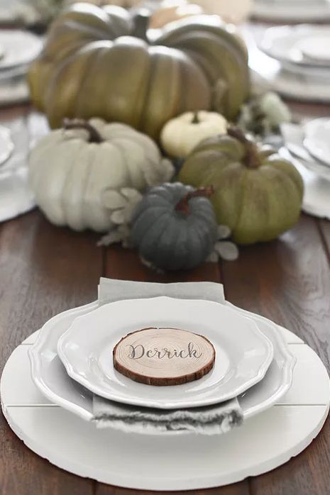 a very simple and stylish Thanksgiving place setting done with a white planked placemat and porcelain, a wood slice and a grye napkin