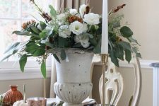 a vintage rustic Thanksgiving centerpiece of an urn with white and rust blooms, greenery and much texture plus a tall and thin candle