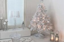 a white and silver living room with a white Christmas tree with lights and silver ornaments, white snowflakes hanging from the ceiling and shiny pillows