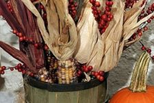 a wooden basket with berries and corn husks plus pumpkins next to it compose a lovely rustic decoration