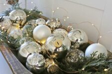 a wooden bowl with silver ornaments, evergreens and lights is a lovely holiday decoration that can be used in various places