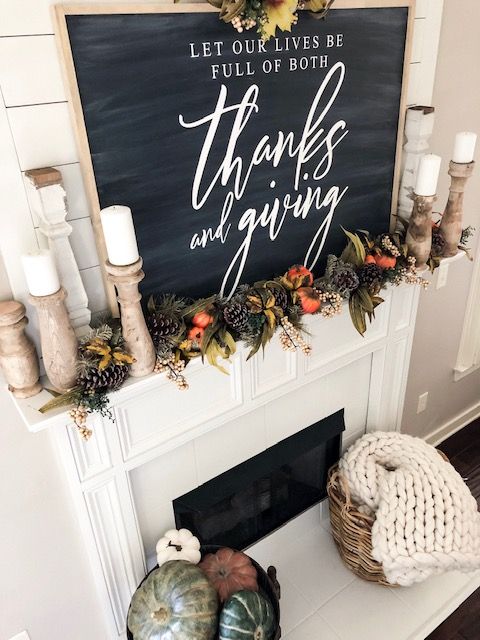 a woodland Thanksgiving mantel with a chalkboard, greenery, pumpkins, pinecones, candles in wooden candleholders